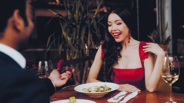 Hispanic Handsome Man Proposing to Girlfriend. Romantic Couple in Love Dating. Cutel Man and Girl in a Restaurant. Romantic Concept. Surprised Attractive Woman Getting a Marriage Proposal. - Foto, afbeelding