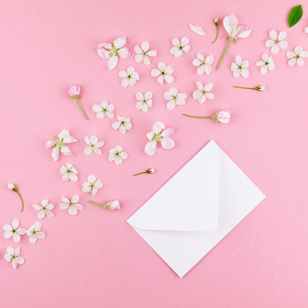 Square flat lay concept top view of blank letter envelope and spring cherry tree flowers on millennial pink background with copy space in minimal style, template for celebration, valentine cards - Photo, Image