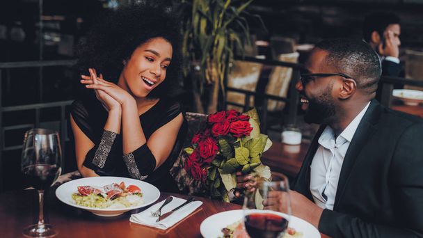 African American Couple Dating in Restaurant. Romantic Couple in Love Dating. Cutel Man and Girl in a Restaurant Making Order. Romantic Concept. Man Giving Bouquet of Flowers. Red Roses. - Foto, Bild