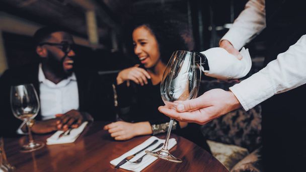 Waiter Pouring Wine to Glass Couple in Restaurant. Romantic African American Couple in Love Dating. Cheerful Man and Woman Drinking Red Wine. Romantic Concept. Anniversary. Bottle of Red Wine. - Foto, Imagem