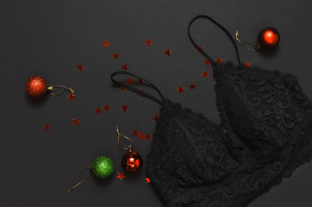 Чорна мереживна бюстгальтерна білизна, різдвяні кульки, голографічна конфетті на темному тлі зверху плоска лежала. Жіночі необхідні еротичні аксесуари, модний подарунок для білизни на Новий рік Різдво
 - Фото, зображення