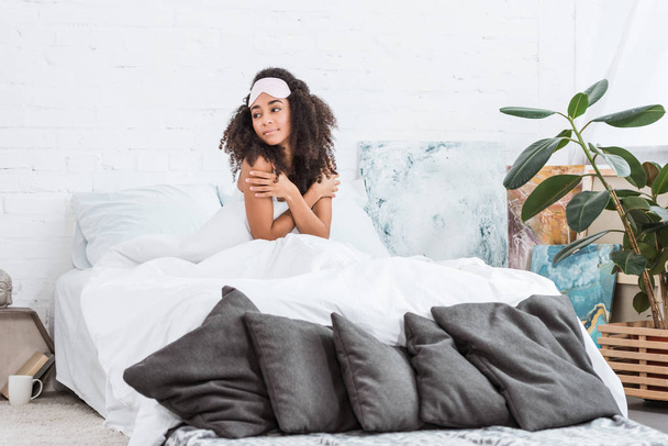 pretty african american woman with blindfold on forehead sitting in bed during morning time at home - Фото, изображение