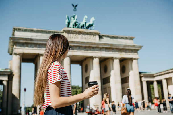 A person holds a disposable cup with coffee or another drink on the background of the Brandenburg Gate in Berlin. - Photo, Image