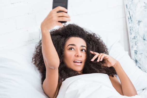 pretty african american girl taking selfie on smartphone in bed during morning time at home - Фото, зображення