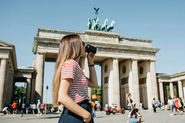 A person holds a disposable cup with coffee or another drink on the background of the Brandenburg Gate in Berlin. - Photo, image