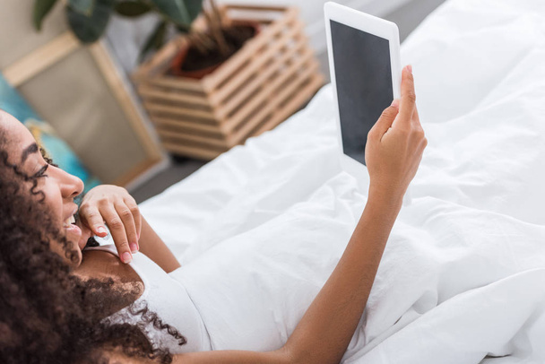 vista lateral de mujer afroamericana usando tableta digital con pantalla en blanco en la cama en casa
 - Foto, imagen