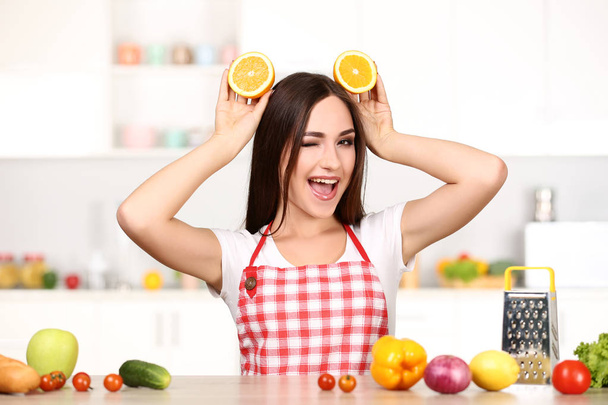 Beautiful woman holding sliced orange fruit and cooking food in the kitchen - Фото, зображення