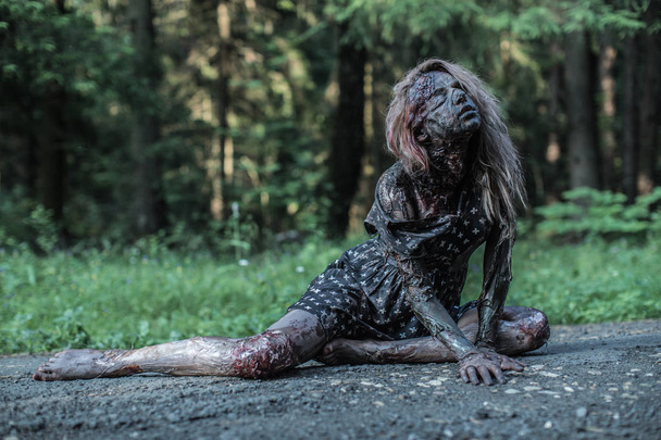 Scary zombie woman lying at forest path - Zdjęcie, obraz