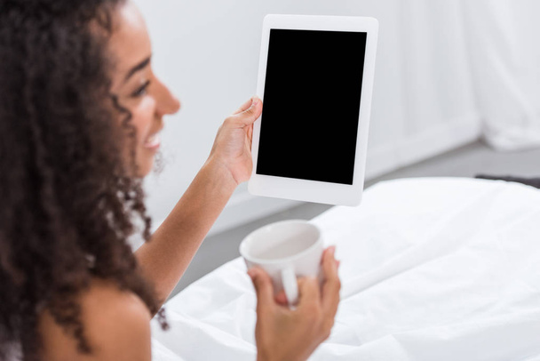 selectieve aandacht van african american vrouw met koffie beker met behulp van digitale tablet in bed thuis - Foto, afbeelding