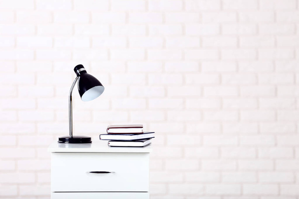 White bedside table with lamp and books on brick wall background - Fotó, kép