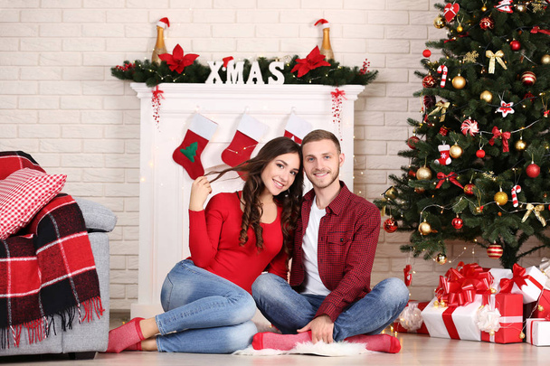 Happy young couple sitting at home near christmas tree - Foto, Bild