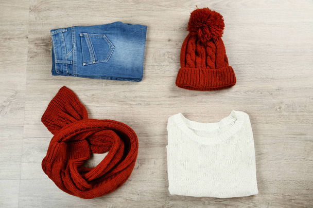 Folded sweater with jeans, hat, and scarf on the floor - Foto, Bild