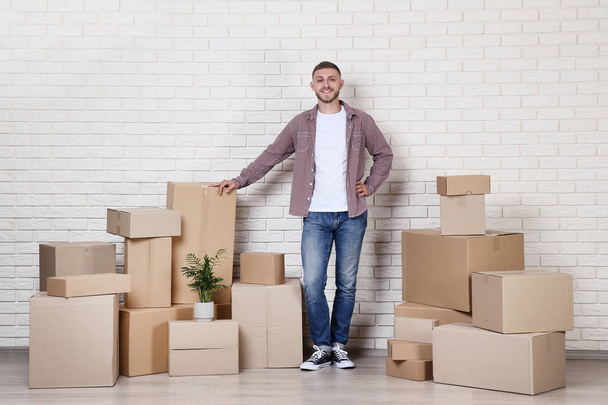 Young man with cardboard boxes on brick wall background - Foto, Imagen