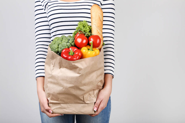 Woman holding grocery shopping bag on grey background - Foto, imagen