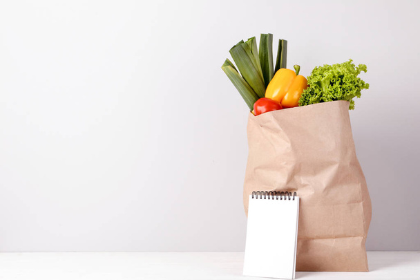 Grocery shopping bag with food and blank notepad on grey background - Fotó, kép