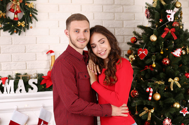 Happy young couple standing at home near christmas tree - Fotografie, Obrázek