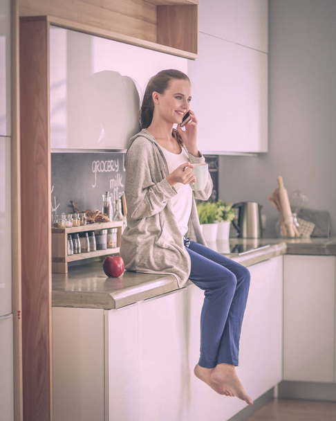 Woman using mobile phone sitting in modern kitchen. - Foto, Bild