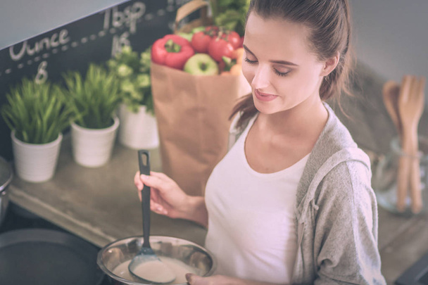 Mujer joven prepara panqueques en la cocina mientras está de pie cerca de la mesa. Mujer en la cocina. Cocinar en la cocina. - Foto, Imagen