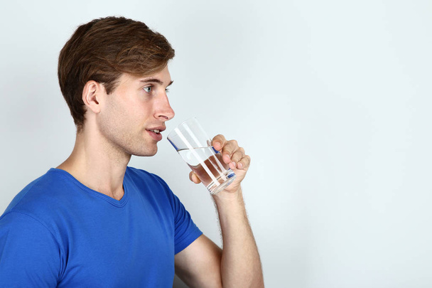 young man drinking water on grey background - Foto, Bild