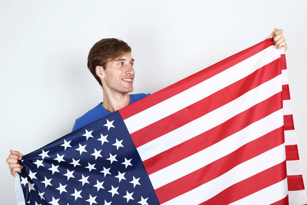 handsome young man holding an American flag on grey background - Photo, image