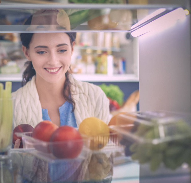 Portrait of female standing near open fridge full of healthy food, vegetables and fruits. Portrait of female - Φωτογραφία, εικόνα