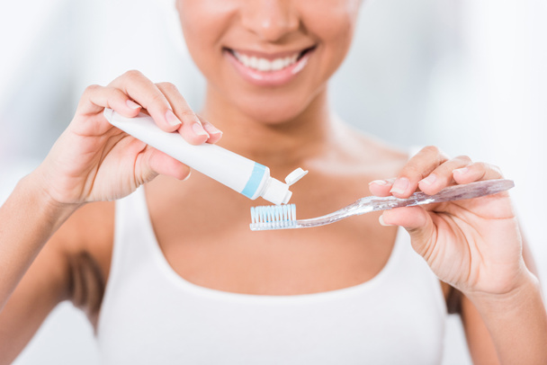 vista parcial de la mujer joven poniendo pasta de dientes en el cepillo de dientes
  - Foto, Imagen