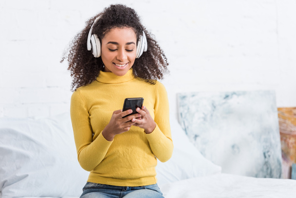 atractiva joven en auriculares escuchando música con teléfono inteligente en casa
 - Foto, imagen