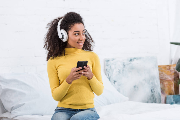 молодая африканская американка в наушниках слушает музыку со смартфоном дома
 - Фото, изображение