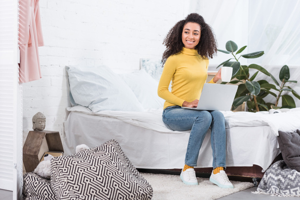 happy african american female freelancer with coffee cup working on laptop at home - Фото, зображення