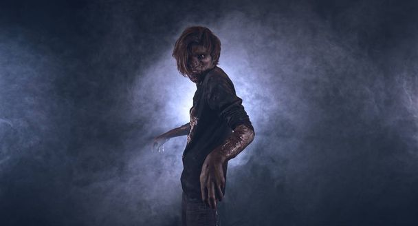 Scary zombie man posing against dark misty background with backlight - Photo, image