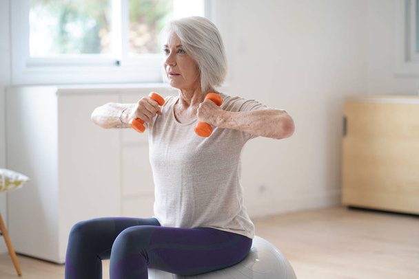  Attractive elderly woman exercising at home with swiss ball                               - Photo, image