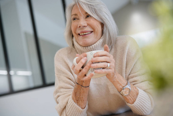  Senior woman at home with hot drink                               - Foto, Bild