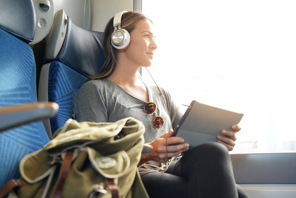 Young woman travelling by train with tablet and headphones                               - Foto, Imagen
