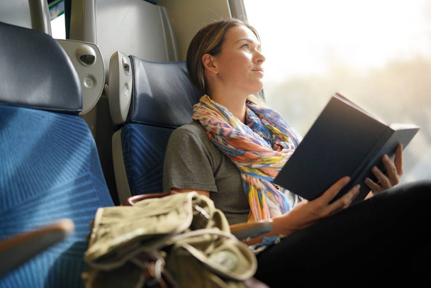 Relaxed young woman reading on the train                                - Valokuva, kuva