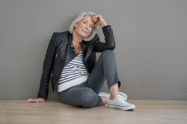  Modern senior woman sitting indoors with leather jacket                               - Foto, imagen