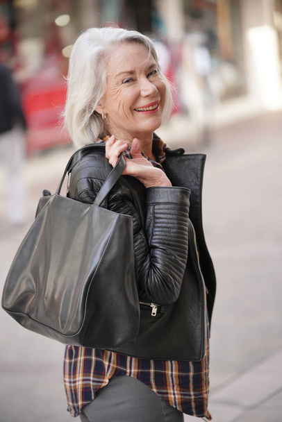  Modern senior woman in town wearing leather jacket                               - Foto, Bild