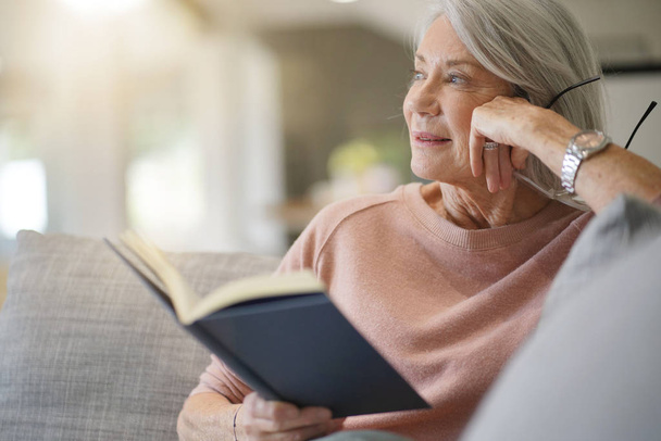  Senior woman reading on couch at home                               - Φωτογραφία, εικόνα