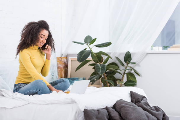 smartphone üzerinde konuşmak ve laptop yatakta evde çalışma Afrikalı-Amerikalı kadın serbest meslek - Fotoğraf, Görsel