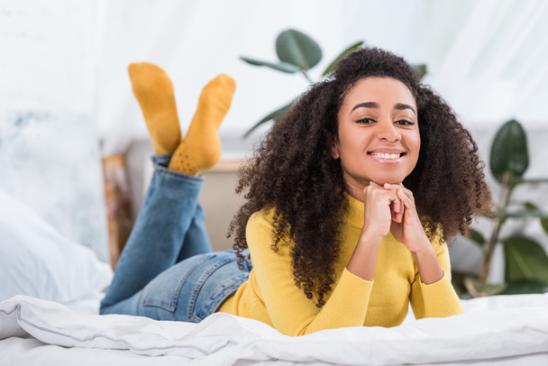 mujer joven afroamericana positiva acostada en la cama y mirando a la cámara
 - Foto, imagen