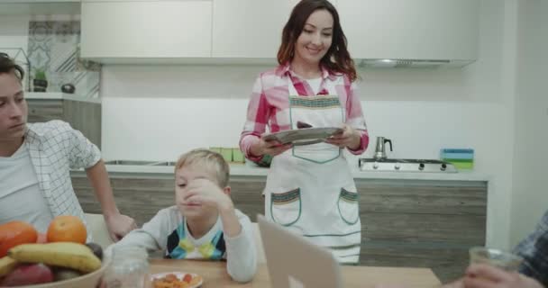 Very attractive mature mother prepare the breakfast for her two boys and husband and happy taking a plate and bringing to the dinner table. - Imágenes, Vídeo