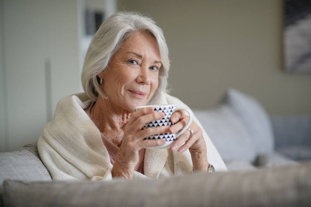  Cosy looking senior woman at home with hot drink                               - Fotoğraf, Görsel
