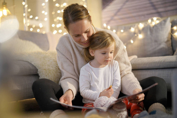  Cosy mother and daughter reading a story at home                              - Фото, зображення