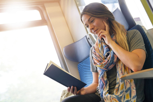 Relaxed young woman reading on the train                                - Фото, изображение