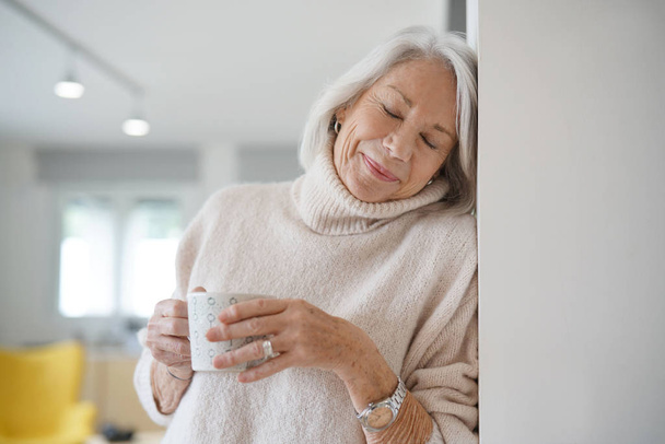  Senior woman at home with hot drink                               - Фото, зображення