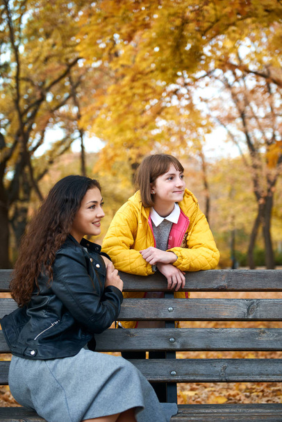 Pretty woman and teen girl are posing in autumn park. Beautiful landscape at fall season. - Foto, Imagem