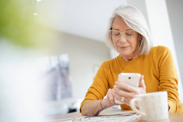 Modern senior woman on cellphone at home                                - Фото, изображение