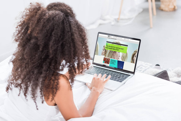 rear view of curly woman using laptop with bbc science on screen in bed at home - Zdjęcie, obraz
