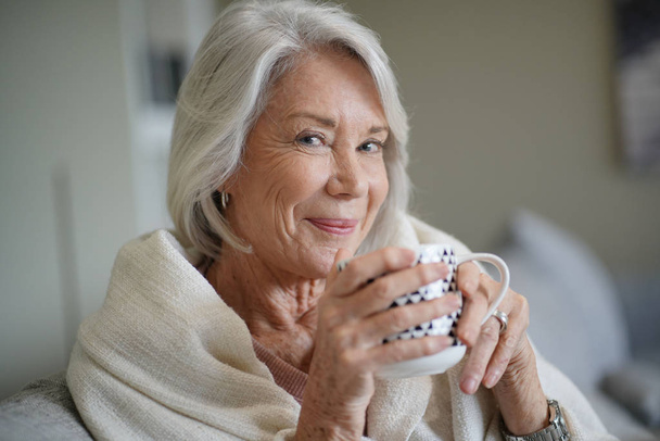  Cosy looking senior woman at home with hot drink                               - Фото, зображення