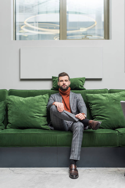homme en tenue formelle avec jambes croisées assis sur un canapé vert et regardant la caméra
 - Photo, image