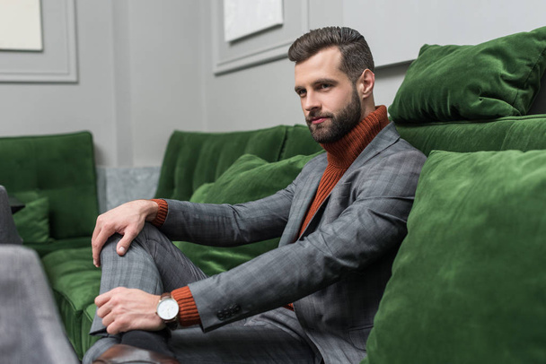 confident man in formal wear with legs crossed sitting on green sofa - 写真・画像